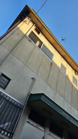 柏原市の戸建て住宅で、ドローンが屋根の真上でホバリングしながらスレートの割れを撮影している写真