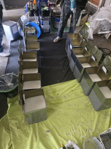 奈良の大阪寄りエリアの現場に並べられた、使い切った下塗り材の一斗缶の山と、笑顔の職人の写真