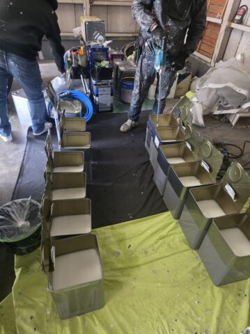 奈良の大阪寄りエリアの現場に並べられた、使い切った下塗り材の一斗缶の山と、笑顔の職人の写真